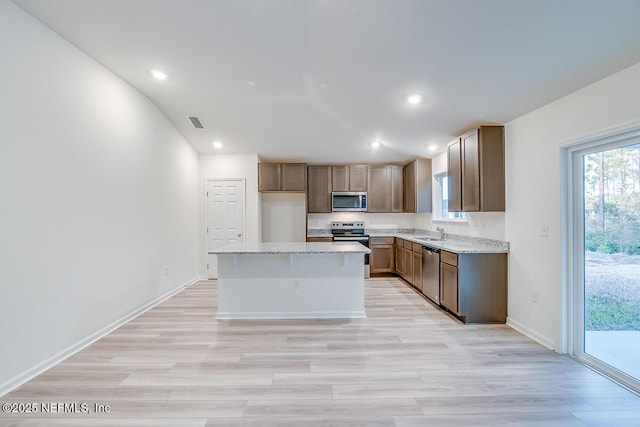 kitchen with sink, stainless steel appliances, a center island, light stone countertops, and light wood-type flooring