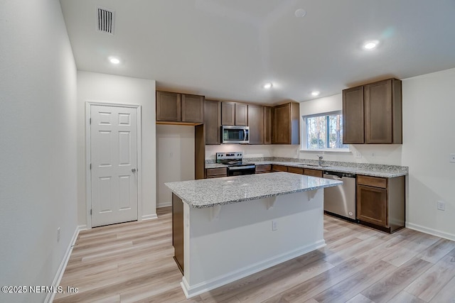 kitchen featuring a kitchen island, appliances with stainless steel finishes, sink, light stone counters, and light hardwood / wood-style floors