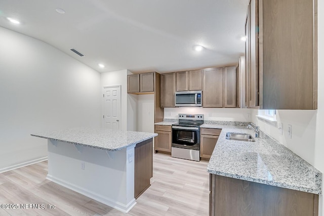 kitchen with sink, stainless steel appliances, a center island, light stone countertops, and light wood-type flooring