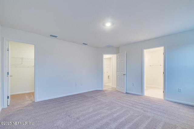 unfurnished bedroom featuring light carpet, a walk in closet, and a closet