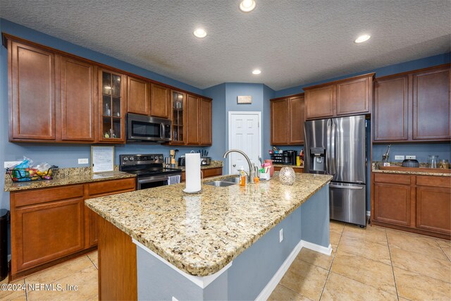 kitchen featuring a center island with sink, light stone counters, sink, and appliances with stainless steel finishes