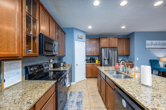 kitchen featuring a textured ceiling, light tile patterned floors, black appliances, sink, and light stone countertops