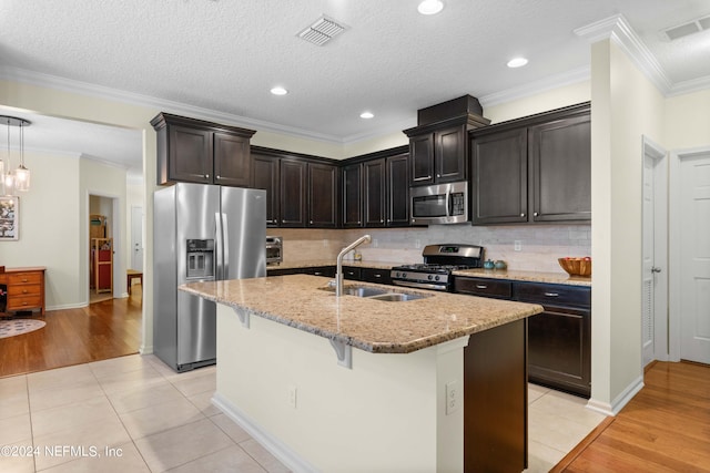 kitchen with light stone counters, crown molding, a kitchen island with sink, light tile patterned floors, and appliances with stainless steel finishes