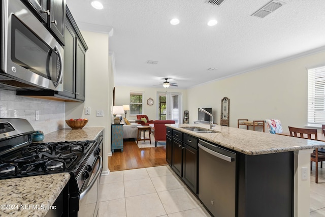 kitchen with sink, ornamental molding, light tile patterned floors, an island with sink, and stainless steel appliances