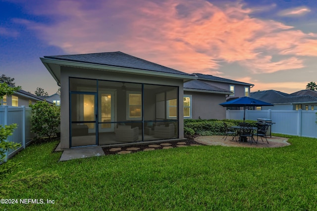 back house at dusk with a yard, a patio, and a sunroom