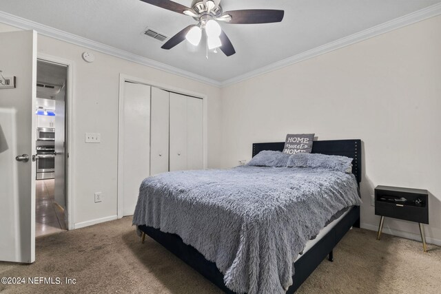 carpeted bedroom with ceiling fan, ornamental molding, and a closet