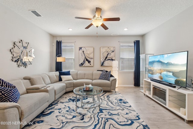 living room featuring ceiling fan, a textured ceiling, and light hardwood / wood-style flooring