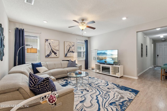 living room with ceiling fan, a textured ceiling, and light wood-type flooring