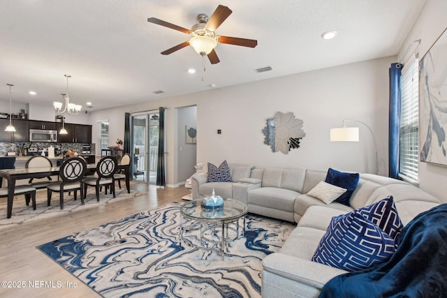 living room featuring ceiling fan with notable chandelier and light hardwood / wood-style floors