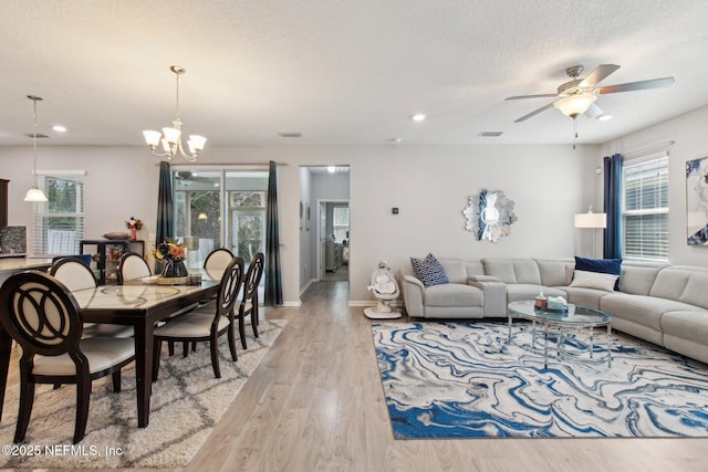 living room featuring ceiling fan with notable chandelier, a textured ceiling, and light hardwood / wood-style flooring