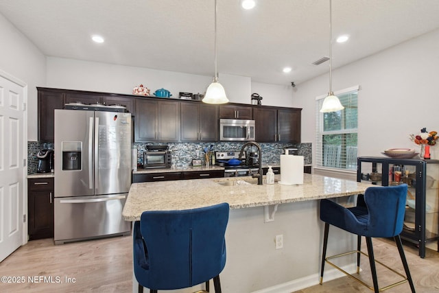 kitchen with appliances with stainless steel finishes, pendant lighting, sink, dark brown cabinets, and a center island with sink