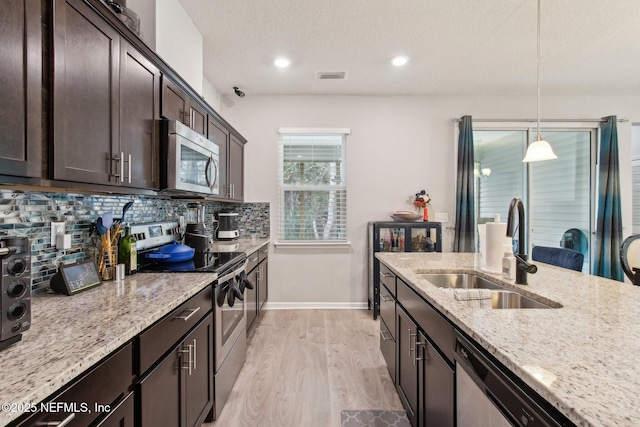 kitchen featuring sink, light stone counters, decorative light fixtures, light wood-type flooring, and stainless steel appliances