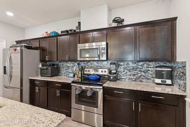 kitchen featuring dark brown cabinetry, backsplash, light stone counters, and stainless steel appliances