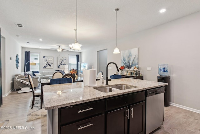 kitchen featuring decorative light fixtures, an island with sink, sink, stainless steel dishwasher, and light hardwood / wood-style floors