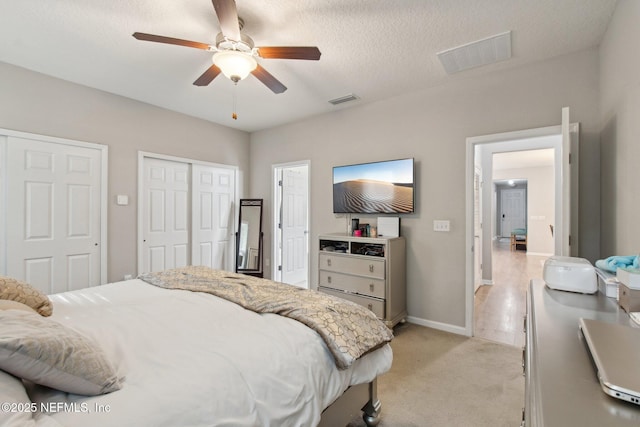 bedroom with multiple closets, ceiling fan, light colored carpet, and a textured ceiling