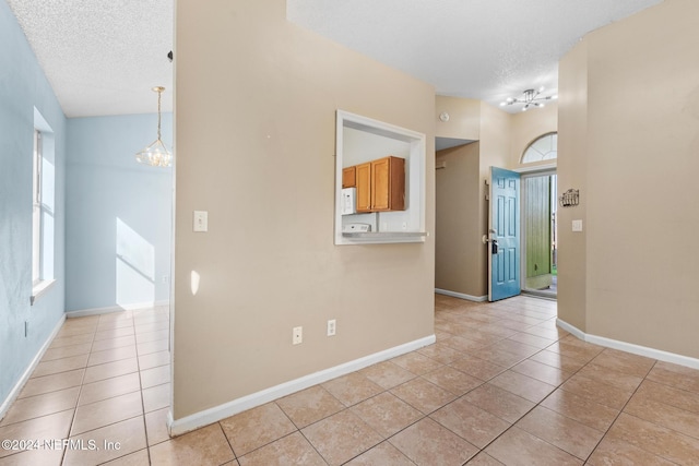 spare room with an inviting chandelier, a textured ceiling, and light tile patterned floors