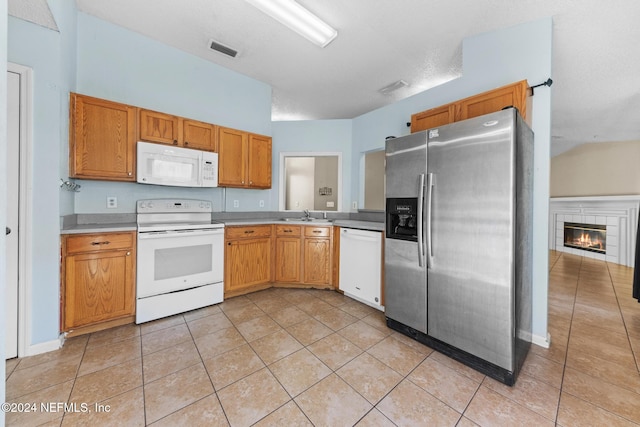 kitchen with sink, a textured ceiling, light tile patterned floors, a tile fireplace, and white appliances