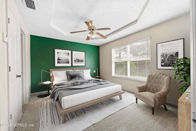 carpeted bedroom featuring ceiling fan, a tray ceiling, and a textured ceiling