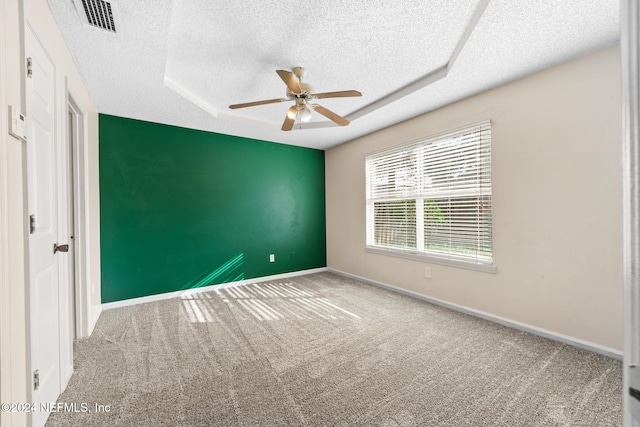 empty room with a raised ceiling, ceiling fan, carpet flooring, and a textured ceiling