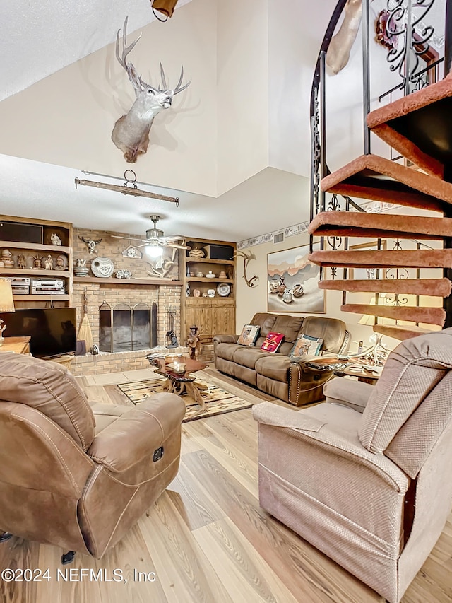 living room featuring built in shelves, a brick fireplace, ceiling fan, hardwood / wood-style flooring, and a towering ceiling