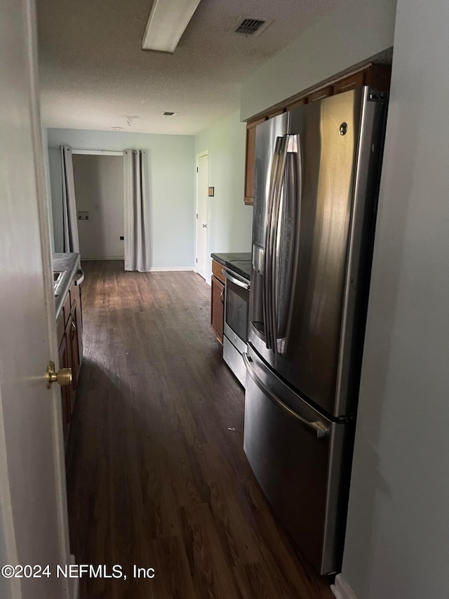 kitchen with a textured ceiling, stainless steel appliances, and dark wood-type flooring