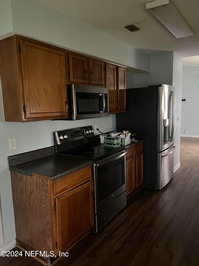 kitchen with stainless steel appliances, a textured ceiling, and dark hardwood / wood-style floors