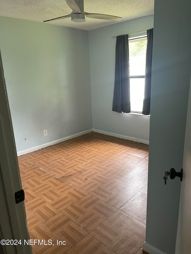 empty room with ceiling fan, light parquet flooring, and a textured ceiling