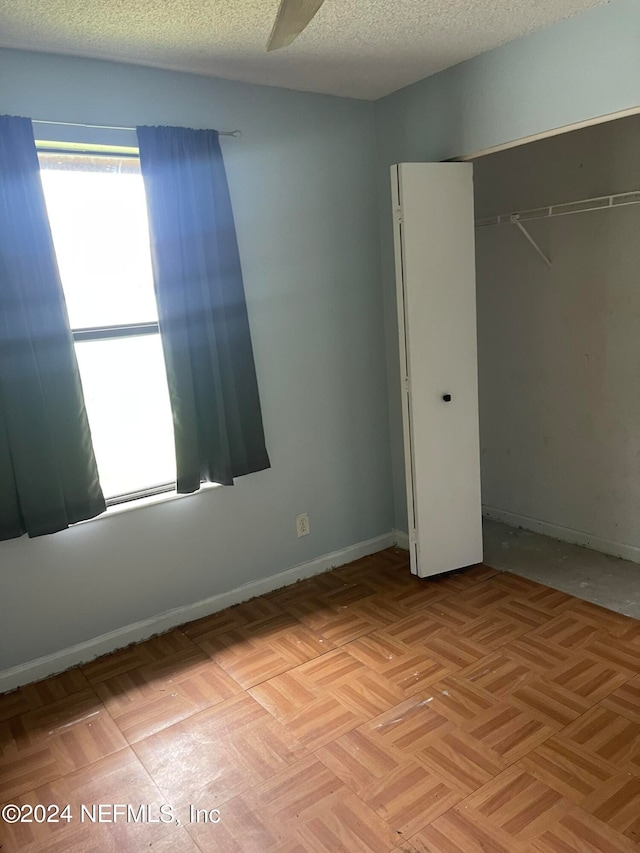 unfurnished bedroom featuring light parquet floors, a textured ceiling, ceiling fan, and a closet