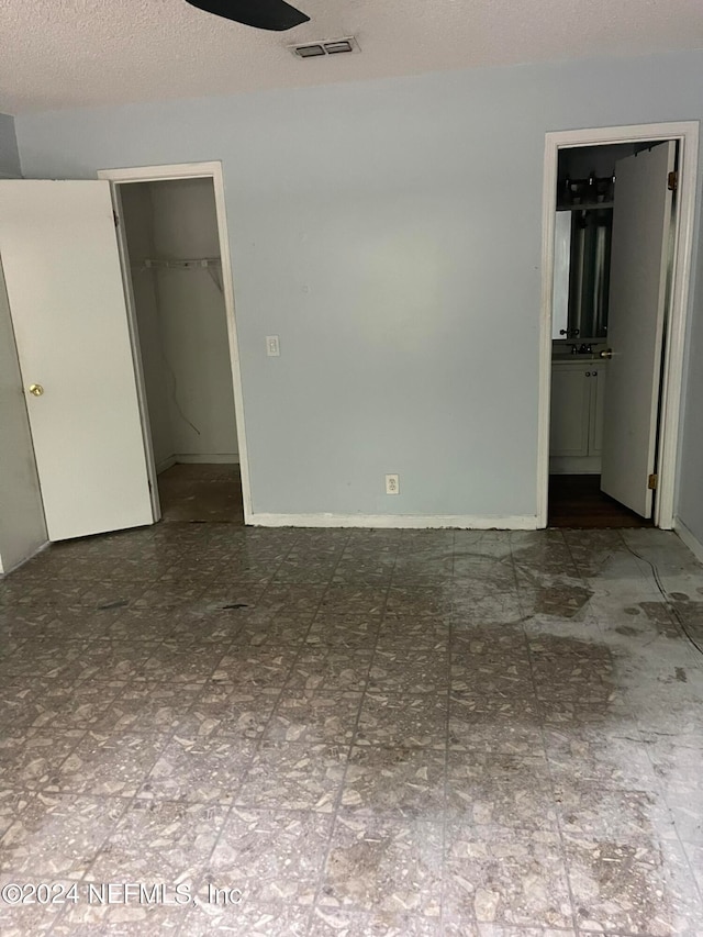 unfurnished bedroom with a textured ceiling, a closet, connected bathroom, and a spacious closet