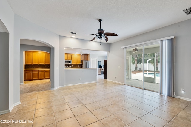 unfurnished living room featuring ceiling fan, light tile patterned floors, and a textured ceiling