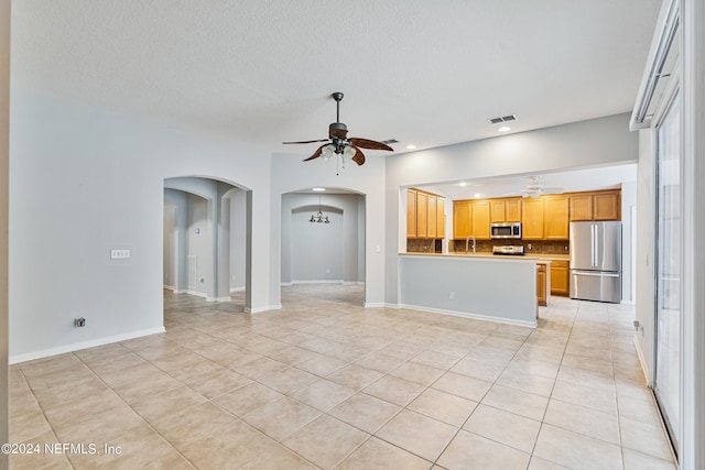 unfurnished living room with a textured ceiling, light tile patterned flooring, sink, and ceiling fan