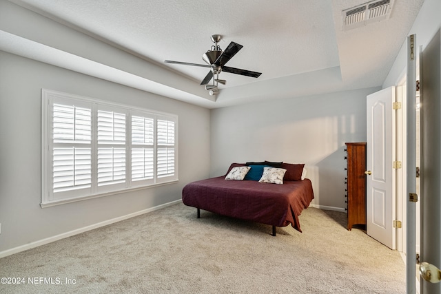 carpeted bedroom with a textured ceiling, a tray ceiling, and ceiling fan