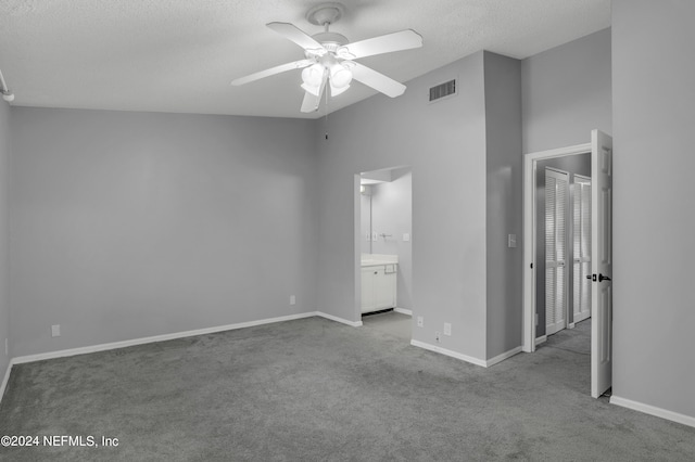 unfurnished bedroom featuring ceiling fan, connected bathroom, a textured ceiling, and light carpet