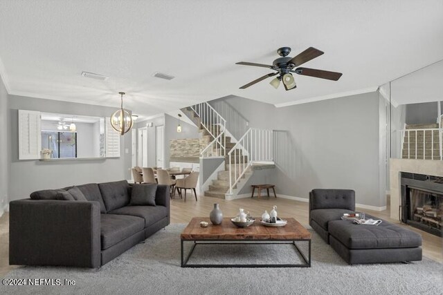 living room with light hardwood / wood-style flooring, ceiling fan with notable chandelier, crown molding, and a tile fireplace