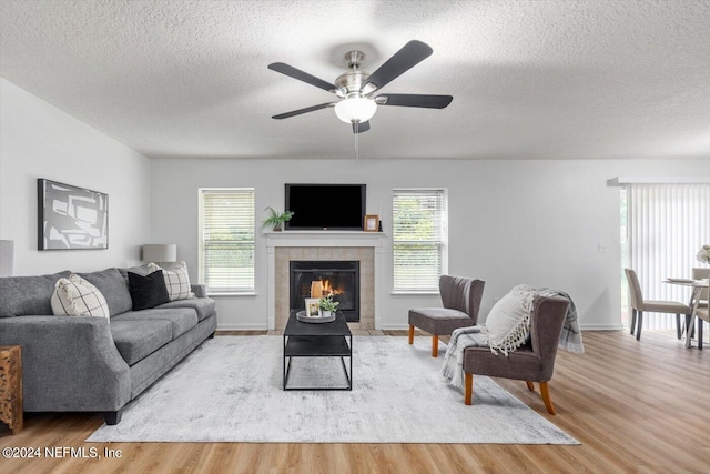 living room with a textured ceiling, a tile fireplace, light hardwood / wood-style floors, and ceiling fan