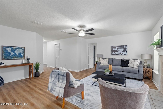 living room featuring ceiling fan, a textured ceiling, light wood-type flooring, and a fireplace