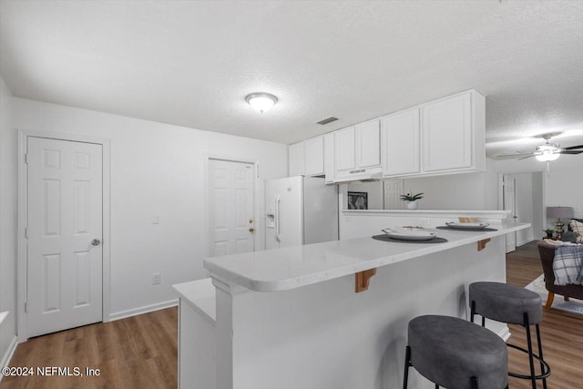 kitchen featuring white cabinetry, dark wood-type flooring, a kitchen bar, ceiling fan, and white fridge with ice dispenser