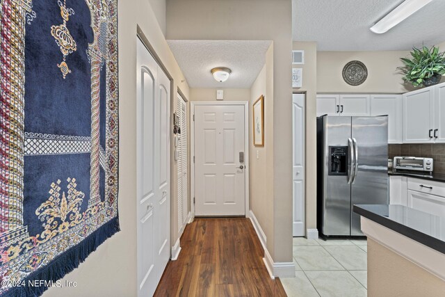 kitchen featuring a textured ceiling, light hardwood / wood-style floors, stainless steel fridge with ice dispenser, and white cabinets