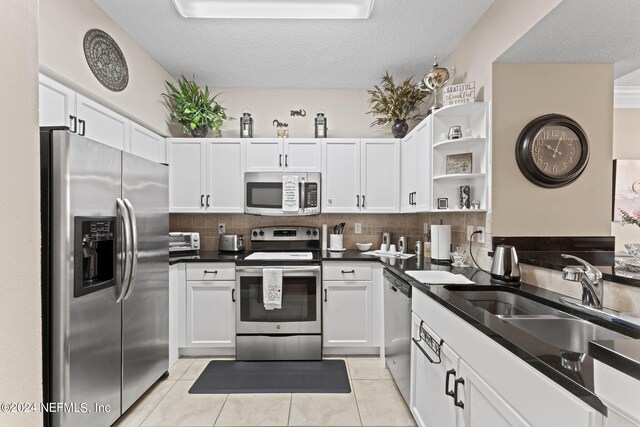 kitchen with appliances with stainless steel finishes, tasteful backsplash, white cabinets, a textured ceiling, and sink