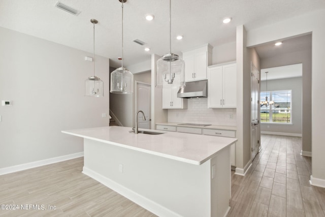 kitchen with hanging light fixtures, white cabinetry, black electric stovetop, a kitchen island with sink, and sink