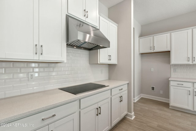 kitchen featuring black electric cooktop, decorative backsplash, light hardwood / wood-style floors, white cabinetry, and a textured ceiling