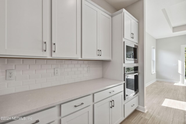 kitchen featuring decorative backsplash, stainless steel appliances, white cabinetry, and light wood-type flooring