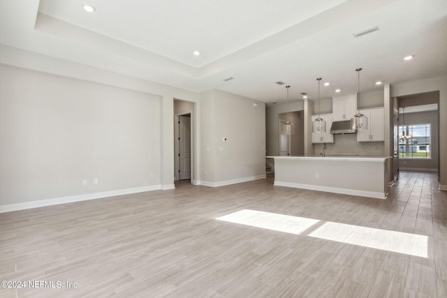 unfurnished living room with light hardwood / wood-style floors and a tray ceiling