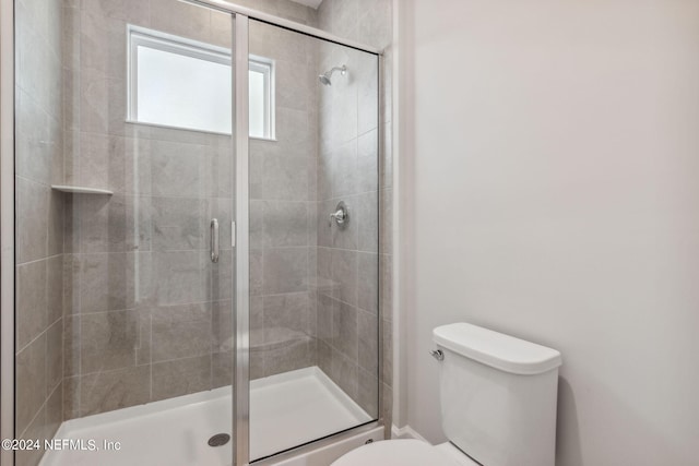 bathroom featuring a shower with shower door and toilet