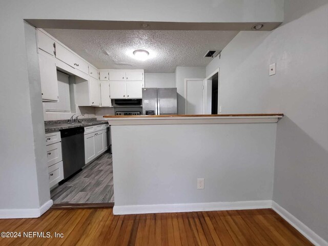 kitchen featuring kitchen peninsula, a textured ceiling, white cabinetry, appliances with stainless steel finishes, and dark hardwood / wood-style flooring