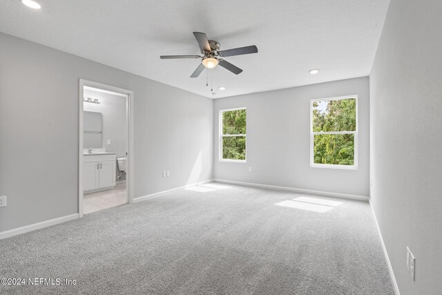 unfurnished bedroom featuring light carpet, sink, ensuite bathroom, and ceiling fan