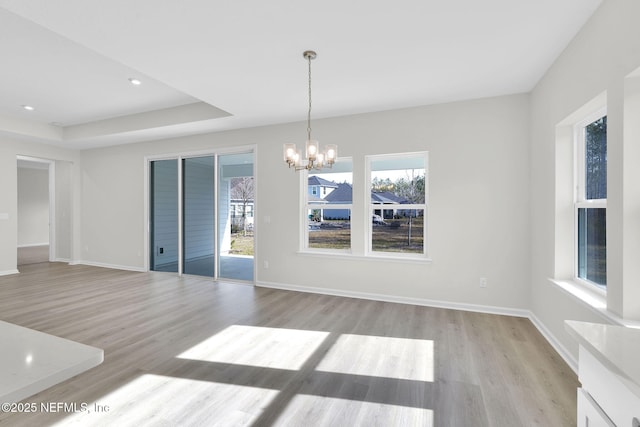 unfurnished dining area featuring a tray ceiling, light hardwood / wood-style floors, and a notable chandelier