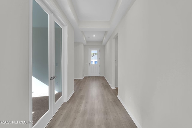 hall with a raised ceiling and light wood-type flooring