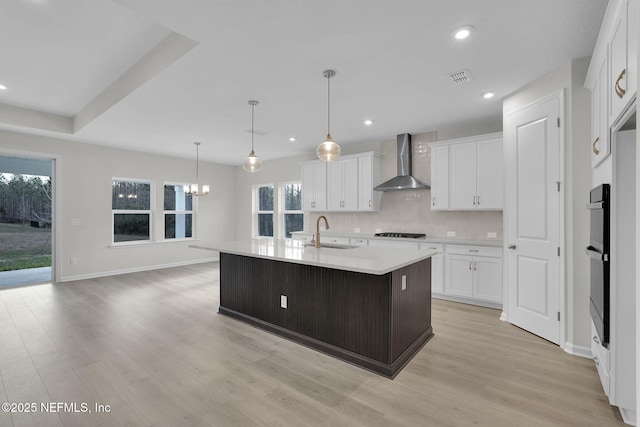 kitchen with white cabinetry, a kitchen island with sink, sink, and wall chimney exhaust hood