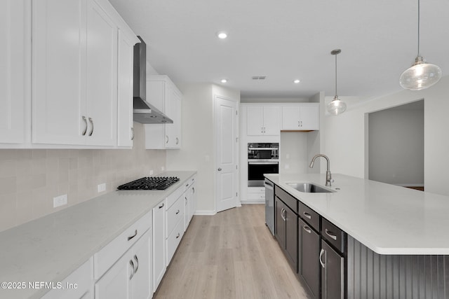 kitchen featuring sink, decorative light fixtures, gas cooktop, a kitchen island with sink, and wall chimney range hood